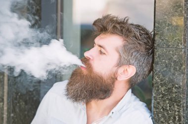 Yan görünümü çekici hipster bir kentsel bağlam ayakta mermer kaplama ile duvar yanındaki adam. İyi görünüyor sakallı adam sigara elektronik sigara, alışkanlıkları ve gençlik moda