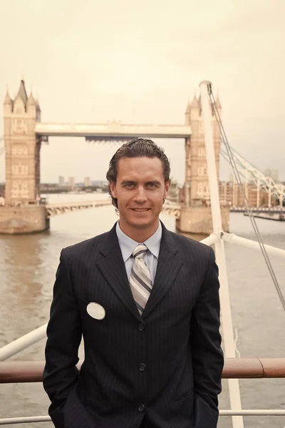 Happy businessman in London, United Kingdom. Man smile at Tower bridge. Tourist enjoy sightseeing in city. Travelling for business and pleasure. Architecture and design concept