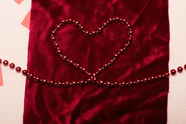 Red beads making heart on scarlet velvet fabric