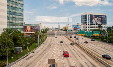 Miami, Amerika Birleşik Devletleri - 30 Ekim 2015: otoyol veya karayolu ile otomobil ve gökdelenler bulutlu mavi gökyüzü üzerinde. Taşıma/iş arabaları için trafik yol işaretleri. Binalar üzerinde reklam panoları. Genel alt yapı kavramı