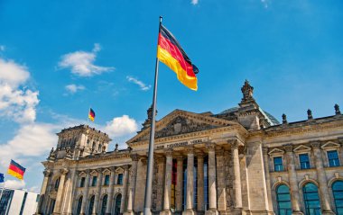 German flags waving in the wind at famous Reichstag building, seat of the German Parliament Deutscher Bundestag , on a sunny day with blue sky and clouds, central Berlin Mitte district, Germany clipart