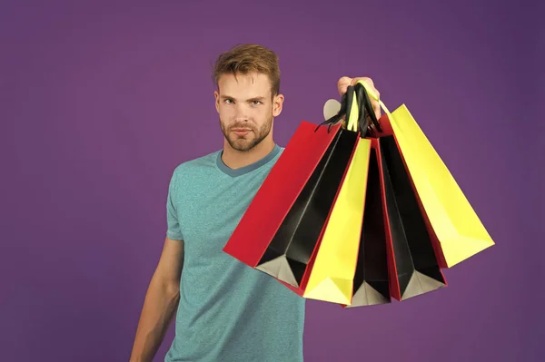 Compras ou venda e segunda-feira cibernética. Homem com sacos de compras em fundo violeta. Macho com sacos de papel coloridos. Comprador de moda em camiseta azul casual. Férias preparação e celebração — Fotografia de Stock