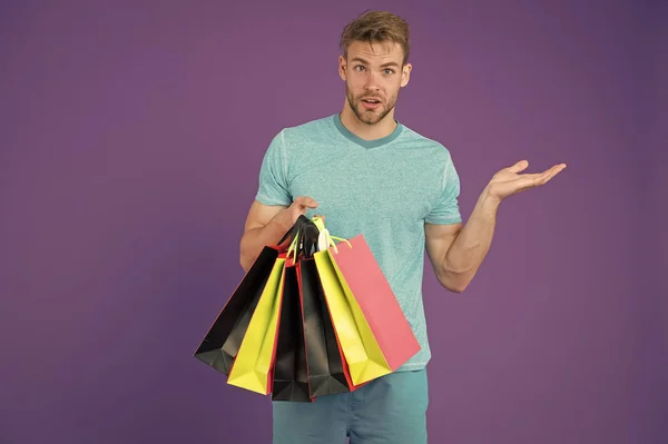 Homem com sacos de compras e gesto de mão sobre fundo violeta. Macho com sacos de papel coloridos. Comprador de moda com sacos de papel. Férias preparação e celebração. Compras e venda, espaço de cópia — Fotografia de Stock