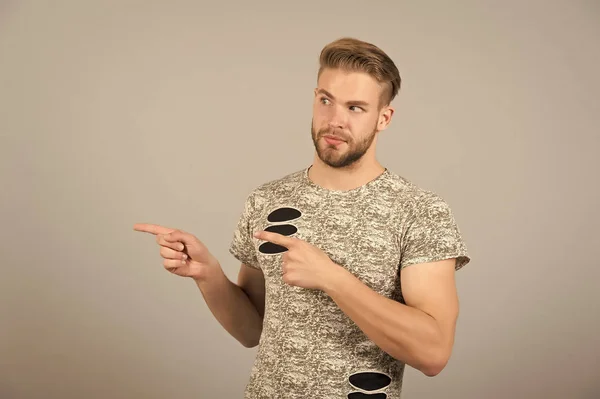 Homem apresentando produto em fundo cinza. Macho com gesto de dedo barbudo. Apresentação, anúncio, anúncio e conceito de promoção, espaço de cópia — Fotografia de Stock