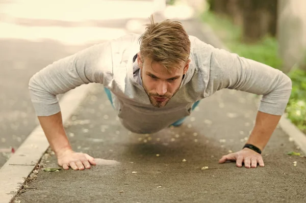 Fuerza y motivación. Hombre en ropa deportiva haciendo flexiones al aire libre. El tipo motivó el entrenamiento en el parque. Deportista mejora su fuerza mediante el ejercicio de empuje hacia arriba. El hombre tiene motivación para el éxito logro deportivo — Foto de Stock