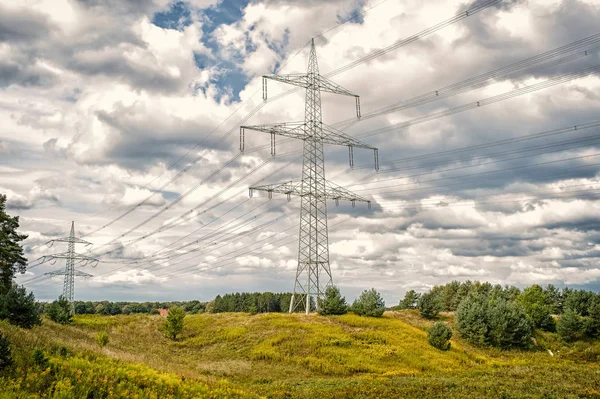 Power towers on natural landscape. Transmission towers on cloudy sky. Electricity pylon structure with power lines. High voltage post outdoor. Energy and ecology