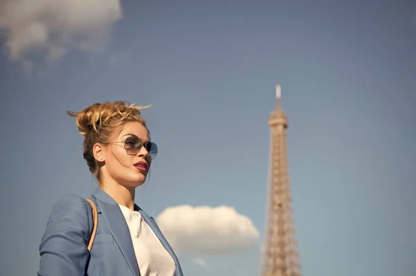 Mulher com maquiagem e óculos de sol em frente ao céu azul e topo da Torre Eiffel no fundo. Conceito parisiense elegante. Senhora no rosto confiante na roupa elegante parece atraente na capital da moda — Fotografia de Stock