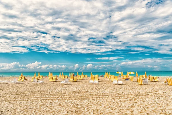 Sillas de playa y sombrillas en el cielo nublado en miami, EE.UU. Playa de mar con arena blanca y agua azul en un día soleado. Vacaciones de verano en el mar o el océano. Wanderlust o viajar y aventura — Foto de Stock