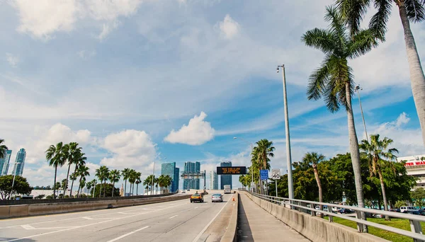 Dálnice nebo silnice s automobily a panorama z miami, usa. Dopravní s dopravní značky pro dopravní prostředky a palmami na modrou oblohou. Koncepce veřejné infrastruktury. Cestování autem — Stock fotografie