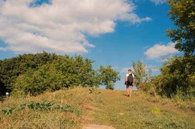 Adam sırt çantası ile güneşli günde tepe üzerinde yürür. Hiking kavramı. Yolcu sırt çantası yürüyüş dağlar, mavi gökyüzü arka plan ile. Adam doğa aşığı zevk yaz'da dağlarda yürüyüş