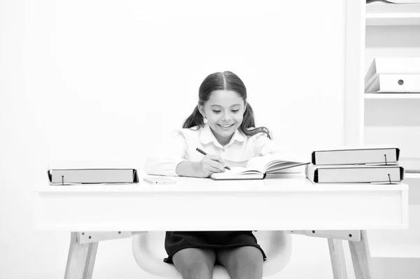 Excelente pupila. Menina criança escreve hometask enquanto sentar tabela fundo branco. Estudante estudando redação escrita. Kid girl escola uniforme rosto feliz faz exercício hometask, espaço de cópia — Fotografia de Stock