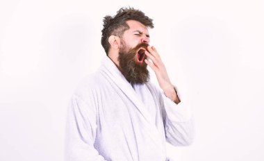 Young man yawning with his mouth wide open. Hipster in white bathrobe isolated on white background. Tired macho in the morning after the party clipart