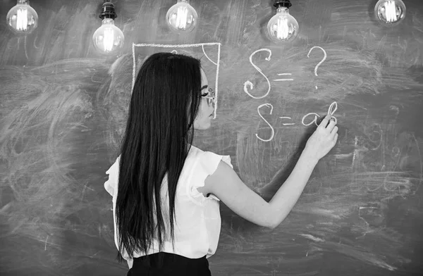 Teacher of mathematics writing on chalkboard, rear view. Sexy teacher concept. Lady sexy teacher in glasses explaining formula. Woman with long black hair teaching mathematics in school