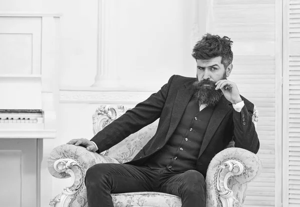 Macho atractivo y elegante en cara seria y expresión reflexiva. Concepto de estilo de vida Elite. Hombre con barba y bigote con traje clásico, se sienta en un sillón a la antigua, fondo blanco — Foto de Stock