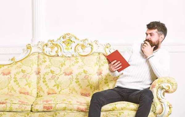Skandal bestseller kavramı. Adam hayretle ile kitap okumak. Sakal ve bıyık oturur barok tarzı kanepe, tutar kitap, beyaz duvar arka plan üzerinde olan adam. Maço sürpriz yüz kitap okuma — Stok fotoğraf