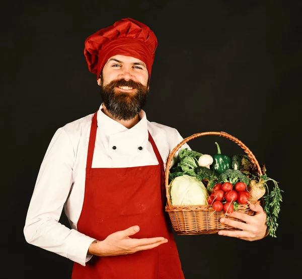 Koch mit Lächeln in weinrotem Hut und Schürze hält Gemüse — Stockfoto