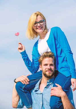 Romantik tarih kavramı. İki açık güneşli gün yürüyüş seviyorum. Adam kız arkadaşı omuzlarında, gökyüzü arka plan taşır. Çift mutlu Tarih birlikte eğleniyor. Kadın kalp aşk sopa sembolü üzerinde tutar.