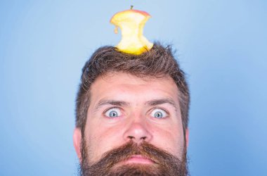 Hipster şok ile elma güdük hedef üzerinde kafa mavi arka plan, yüz kadar yakın. Adam yakışıklı hipster uzun sakal neredeyse kafasına elma güdük hedef olarak yem. Kilo kaybı gol. Canlı hedef kavramı