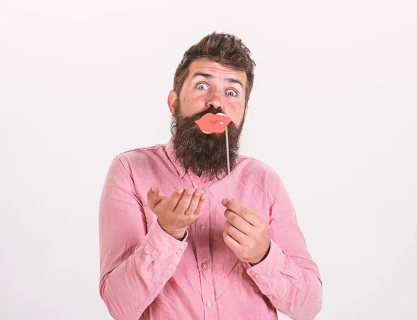 Photo booth fun concept. Man holding party props lips, white background. Hipster with beard and mustache on cheerful face posing with photo booth props, copy space. Guy sending air kiss with red lips — Stock Photo, Image