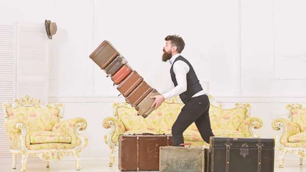 Gepäckversicherung. Mann mit Bart und Schnurrbart im klassischen Anzug liefert Gepäck, luxuriöses weißes Interieur. Portier, Butler stolperte versehentlich und ließ Stapel alter Koffer fallen — Stockfoto