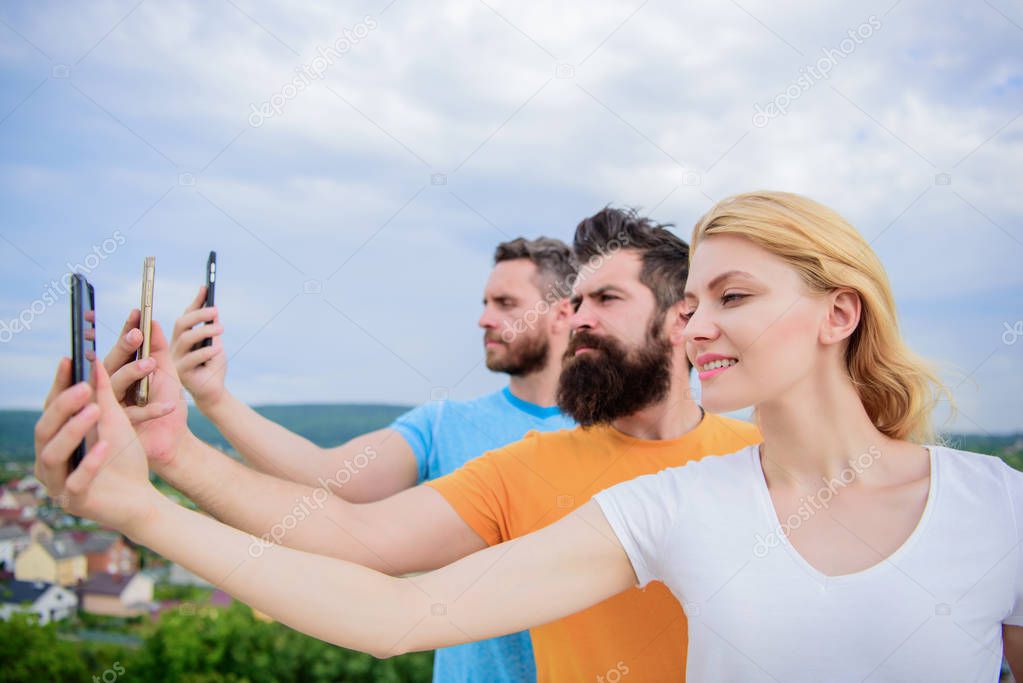 Sharing selfie on social network. Best friends taking selfie with camera phone. Pretty woman and men holding smartphones in hands. People enjoy selfie shooting on nature. A form of self expression