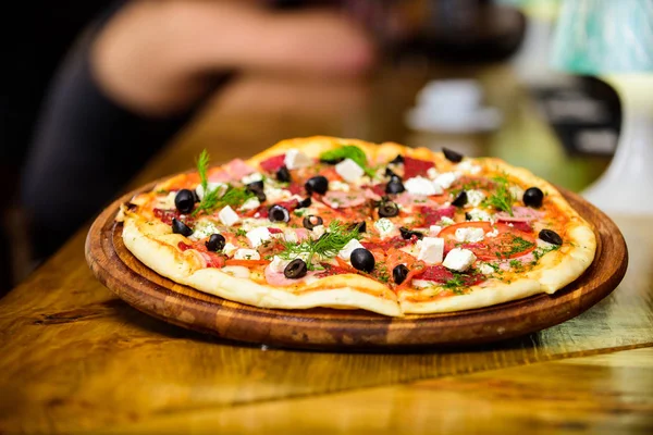 Pizza with tomatoes black olives and ham. Take away food concept. Pizzeria restaurant. Italian pizza concept. Delicious hot pizza on wooden board plate. Food delivery service. Pizza served with dill — Stock Image Pizza with tomatoes black olives and ham. Take away food concept. Pizzeria restaurant. Italian pizza concept. Delicious hot pizza on wooden board plate. Food delivery service. Pizza served with dill Royalty Free Stock Images