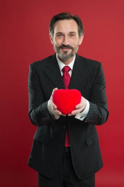 Aşk yayıldı. Olgun yakışıklı adam giyim şık takım elbise kırmızı kalp tutun. Sevgililer günü kutlama. Romantik sürpriz. Sevgililer Günü'nü kutluyorlar. Sevgililer günü için hediye hazırlamak. Aşk tarihi yıldönümü