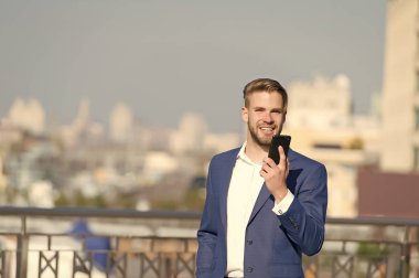 Güneşli terasta akıllı telefonu olan mutlu bir iş adamı. Dışarıdaki cep telefonuyla resmi takım elbiseli bir adam gülümsüyor. İş iletişimi ve yeni teknoloji. İş hayatı konsepti