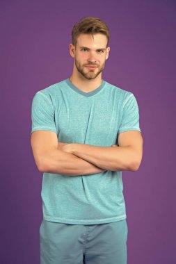 Üzerinde güvenle katlanmış silah, menekşe arka plan ile poz yüzü gülen adam. Kıl adamla sportif giysiler dizi giyer. Moda kavramı. Erkek gömlek ve pantolon sportif kümesinde çekici görünüyor