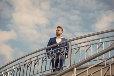 İş adamı çekici görünüşü başarılı görünüyor. Özgürlük kavramı. Kendine güvenen ve bakımlı bir adam özgürlüğün tadını çıkarır. Takım elbiseli başarılı bir girişimci açık havada güneşli bir günde, gökyüzü arka planında yürür.