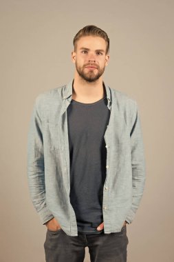 Katı sakallı adam günlük kıyafetler giyer, gri arka plan. Tıraşsız sakallı adam yakışıklı ve bakımlı görünüyor. Sakallı, çekici ve saç stili olan adam. Erkeklik kavramı