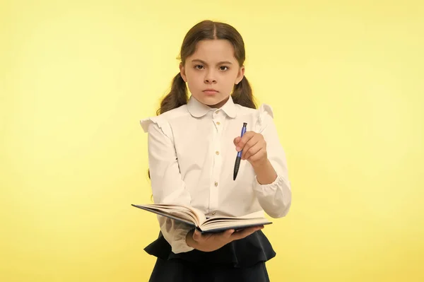 女孩可爱严肃的脸黄背景。女童军校服装着书和笔。检查我的作业。儿童校服聪明的孩子做完作业。检查知识概念 — 图库照片