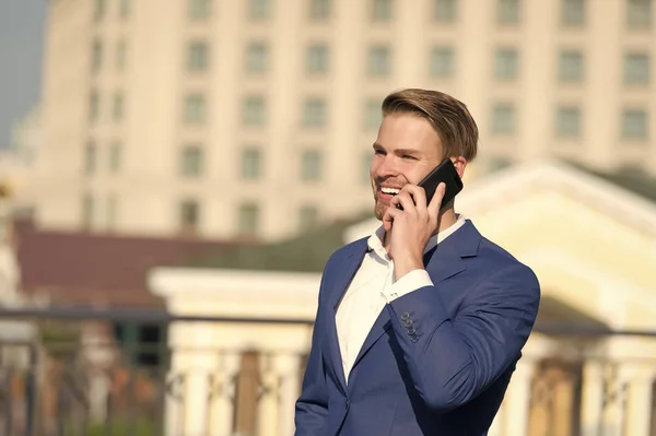 Comunicación empresarial y nuevas tecnologías. Feliz hombre de negocios con smartphone en terraza soleada. Hombre sonrisa en traje formal con teléfono móvil al aire libre. Concepto de estilo de vida — Foto de Stock