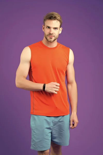 Man with sport smartwatch on violet wall. Sportsman in orange vest and blue shorts. Fashion accessory for training and workout. New technology for healthy lifestyle. Sport or fitness and wellness — Stock Photo, Image
