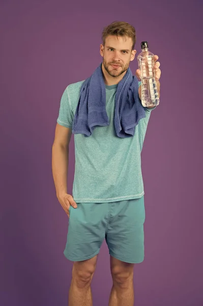 Homme tenir bouteille d'eau sur fond violet. Sportsman avec bouteille en plastique au mur violet. Athlète en t-shirt bleu et short avec serviette après l'entraînement. Soif et déshydratation. Activité sportive et énergie — Photo