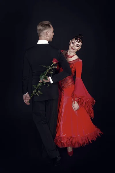 Sensual woman and man dance with rose flower. Woman in red dress and macho in tuxedo. Couple of ballroom dancers in love. Valentines day celebration. Love proposal and date concept