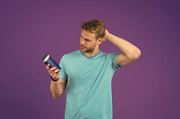 Homme au visage confiant touchant ses cheveux, fond violet. Le gars à poils tient une bouteille avec shampooing, espace de copie. Homme profiter de la fraîcheur après avoir lavé les cheveux avec un shampooing. Soins capillaires et concept de shampooing — Photo