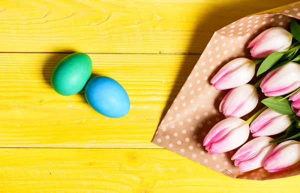 A Páscoa está a chegar. Ovos coloridos brilhantes e flores de tulipa fresca bouquet no fundo amarelo vista superior. Férias. A tradição celebra a Páscoa. Feliz época de Páscoa. Símbolo de ovos de Páscoa. Vibrações de primavera — Fotografia de Stock