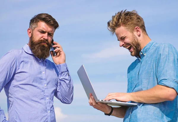 Business team works outdoor, sky background. Men with laptop and smartphone solving problems using mobile internet. Workers with gadgets always having access to mobile internet. Always online.