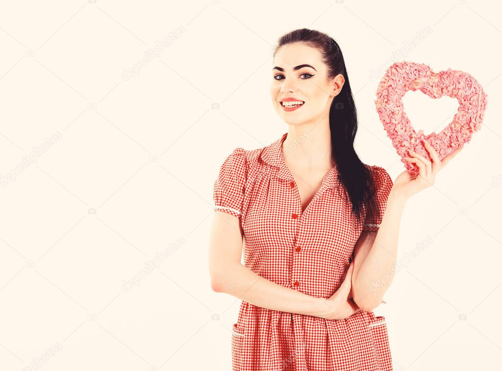 Lady wears fashionable clothes in love. Girl with happy face, make up and pink heart. Woman in stylish dress holds symbol of love and smiles. Flirt, present, style, Valentines day, happiness concept