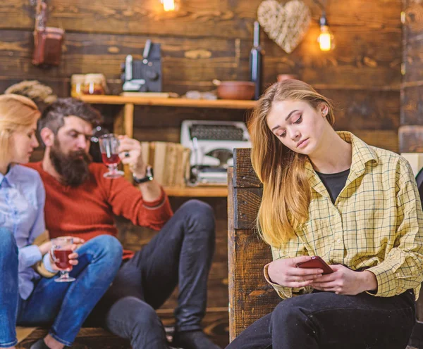 Teenage girl checking smartphone, virtual reality vs real life concept. Bearded man chatting with his blond wife while drinking wine or punch. Daughter spending time on her own without parents