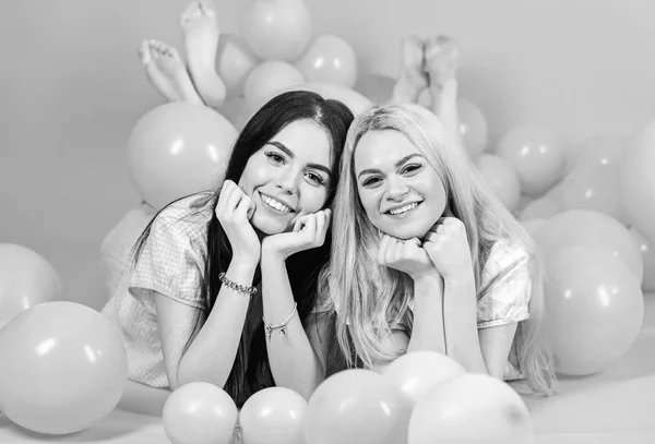 Morena y rubia mujeres lindas en pijama rosa posando en la cámara mientras yacía cerca de globos aéreos en la fiesta de pijamas sobre fondo rosa —  Fotos de Stock