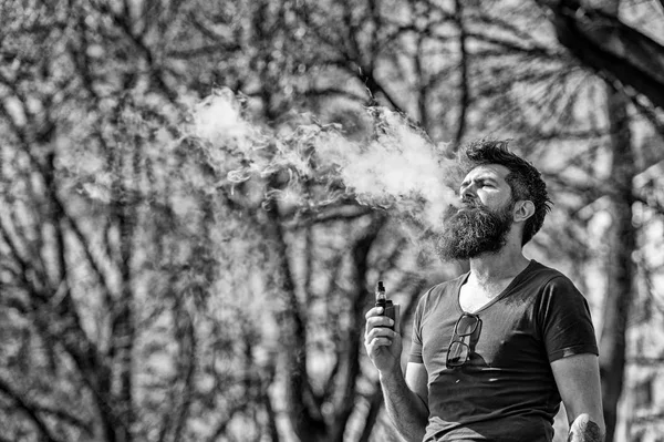 Homem barbudo fumando e-cigarro ao ar livre. Homem elegante passeando na cidade exalando vapor. Cigarros electrónicos como alternativa ao tabaco — Fotografia de Stock