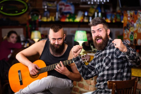 Cheerful friends sing song guitar music. Relaxation in pub. Friends relaxing in pub. Live music concert. Man play guitar in pub. Acoustic performance in pub. Hipster brutal bearded with friend in pub