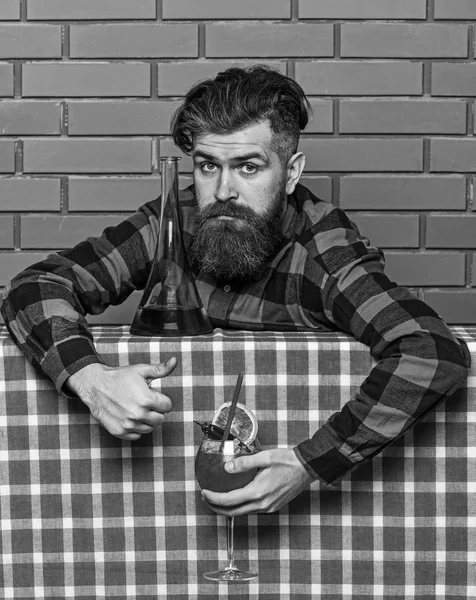 Bartender concept. Man in checkered shirt on brick wall background. Barman with long beard and mustache and stylish hair on calm face, made alcoholic cocktail, shows thumbs up gesture