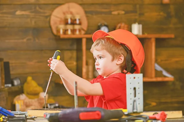 Seitenansicht kleines Kind, das Schraube in Holzbrett bindet. Konzentrierter Junge, der mit Schraubenzieher spielt. Kleiner Bauarbeiter in der Werkstatt — Stockfoto