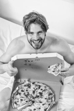 Adam yakışıklı adam yatakta kahvaltı için peynirli yemek yeme sakallı. Adam, kahvaltıda pizza seviyor. İç çamaşırı aç genç adam evde pizza kutusu ile bir yatakta oturur. Yatak pizza.