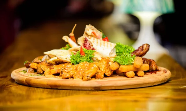 Enjoy your meal. Pub menu snack. Meat snack for group friends. Tasty delicious snacks. Snack for beer. Restaurant food. Wooden board french fries fish sticks burrito and meat steak served with salad