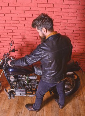 Yenilikçi, vahşi motorcu deri ceketli motosiklet üzerinde arka görüş oturur. Sakallı, motorcu motorlu bisiklet garaj, tuğla duvar arka plan yakınındaki deri ceketli adam. Erkeksi hobi kavramı
