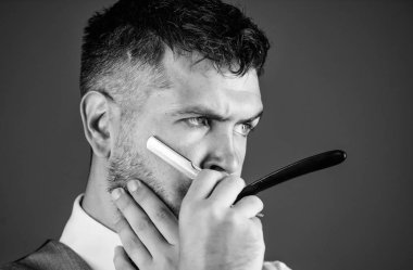 Erkek yelek papyon ile usturanın mavi arka plan tutun. Kuaför sanat kavramı. Kuaför keskin tehlike ustura ile tıraşsız hippi. Berber Kuaför Salonu. İpuçları bakım Kuaför sakal